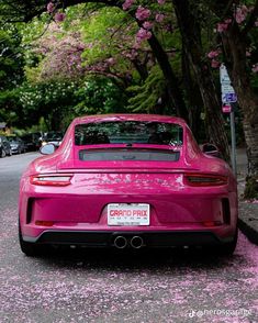 a pink sports car parked on the side of the road in front of some trees