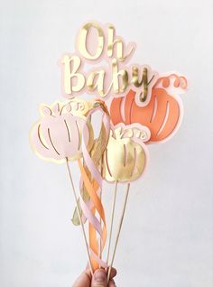 a person holding up some cake toppers with the words oh baby on them and pumpkins