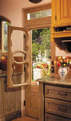 a vase with flowers sitting on top of a counter in front of a window next to a wooden cabinet