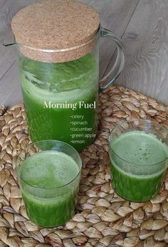 two glasses filled with green liquid sitting on top of a woven place mat next to a jug