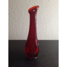 a red glass vase sitting on top of a black table next to a white wall