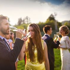 a man and woman are drinking from wine glasses at an outdoor wedding party with other people in the background