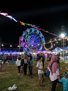 many people are walking around in the grass at an amusement park with lights and rides