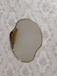 an oval mirror on the wall with flowers and vines around it, in front of a floral patterned wallpaper