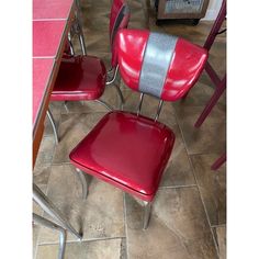 two red chairs sitting next to each other on a tile floor in front of a table