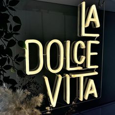 a neon sign that says la dolce vita on the side of a wall next to plants