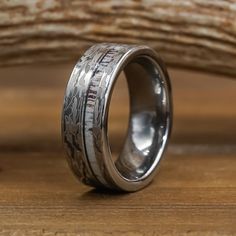 a wedding ring with silver lettering on it sitting on top of a wooden table next to a piece of driftwood