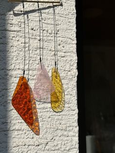 three different colored glass pieces hanging from hooks on a white brick wall next to a window