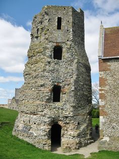 an old stone tower sitting in the middle of a grass covered field next to a building