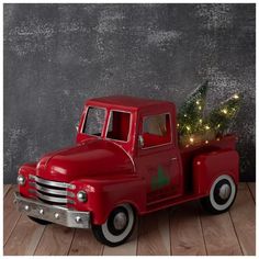 an old fashioned red truck with a christmas tree in the back and lights on it