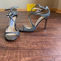 - Designer = Jimmy Choo London - Size = 10.5m (40.5). Trunk 24 - Msrp = $850 - Color = Glittery Gray. - Style = Textured Glittery Gray Genuine Leather Women’s Size 10.5m Strappy Open Toe Stiletto Heel Sandals8 - Made In Italy . - Heel Height = 4” Inches Glossy Gray Stilettos Heel. - Padded Leather Insole And Leather Outsole5 - Measured From Inside, From Front Tip Of Open Toe To Back Tip Of Heel To Give An Estimate Of Size Length =Approximately 26.1cm. - Perfect Item For Work And Formal Evenings. Luxury Glitter Sandals With Ankle Strap, Luxury High Heel Glitter Sandals, Luxury High Heel Sparkling Sandals, Luxury Open Toe Sparkling Sandals, Luxury Sparkling High Heel Sandals, Luxury Sparkling Open Toe Sandals, Luxury Sparkling Sandals For Gala, Luxury Formal Sandals With Glitter, Luxury Glitter Sandals For Formal Occasions