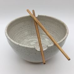 two chopsticks sticking out of a white bowl with speckled glaze on it