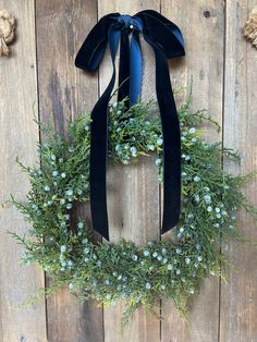 a wreath hanging on the side of a wooden wall with blue ribbon and green flowers