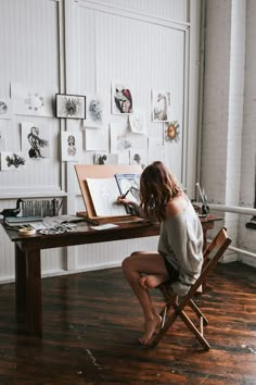 a woman is sitting at a desk in front of an easel with drawings on it