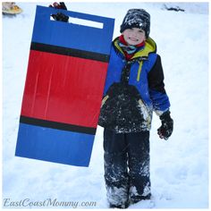 a young boy standing in the snow next to a blue and red sledder