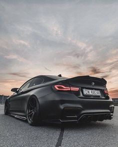 the rear end of a black car parked on top of a parking lot at sunset