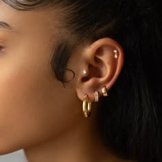 a close up of a person with ear piercings on their ears and wearing gold jewelry