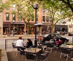 people are sitting at tables outside on the sidewalk