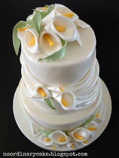 a three tiered cake with white and yellow flowers on the top, sitting on a plate