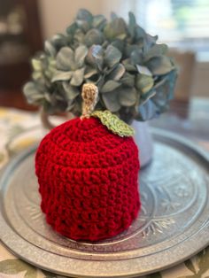 a crocheted red apple sitting on top of a silver plate