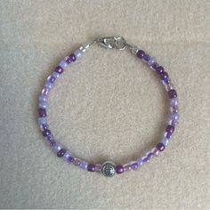 a beaded bracelet with purple beads and a silver charm sits on a carpeted surface