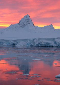 the sun is setting over an iceberg in the ocean with pink sky and clouds