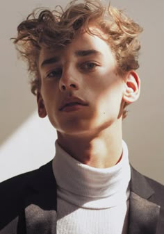 a young man with curly hair wearing a suit and turtle neck sweater