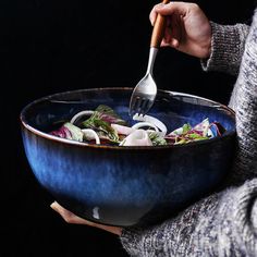 a woman is holding a large bowl full of food with a fork in her hand