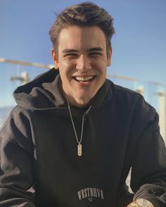 a young man sitting on top of a motorcycle wearing a black hoodie and smiling at the camera