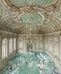 several people are swimming in a large indoor pool with intricate designs on the walls and ceiling