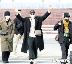 three men wearing face masks walking down the street with their hands up in the air