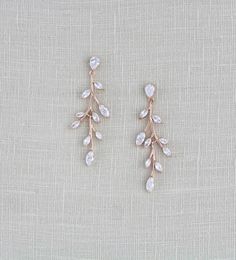 two pairs of gold tone earrings with white stones and leaves on the front, set against a beige linen background