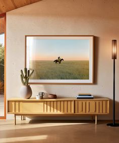 a painting hangs on the wall next to a table with a vase and potted plant