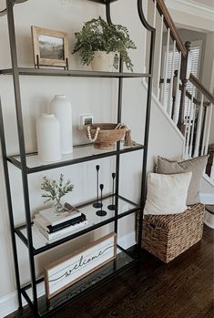 a shelf with books and plants on it next to a stair case in a home