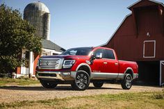 a red pickup truck parked in front of a barn and silo on a farm