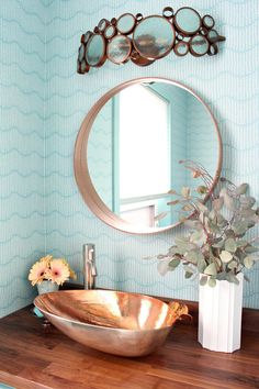 a bathroom sink sitting under a round mirror next to a vase with flowers in it