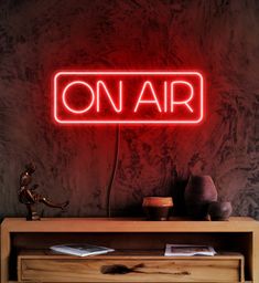 a red neon sign that reads on air above a wooden cabinet with vases and other items