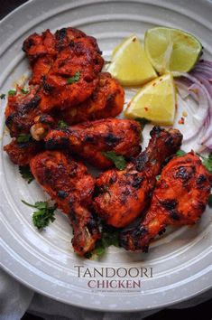 grilled chicken on a white plate with lemon wedges and cilantro