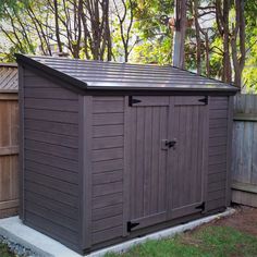 a brown storage shed sitting in the middle of a yard next to a wooden fence