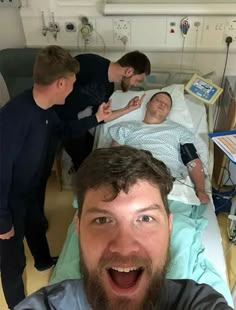 a man in a hospital bed with two other men around him looking at the camera