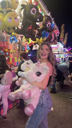 a woman holding a teddy bear in front of a carnival booth with balloons and decorations