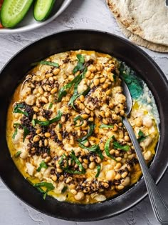 a pan filled with food next to cucumbers and pita bread