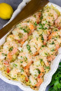 a casserole dish filled with shrimp and cheese next to parsley on a table