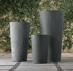 three tall vases sitting next to each other on top of a stone floor in front of trees