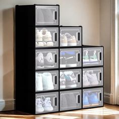 a stack of six clear boxes filled with pairs of shoes sitting on top of a hard wood floor