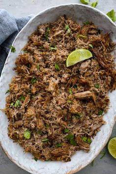 shredded pork in a white bowl with limes and cilantro on the side