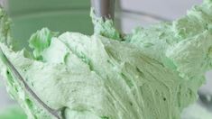 a green frosted cake in a glass bowl with a metal spoon on the side