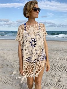 a woman walking on the beach wearing a crochet ponchy coverup