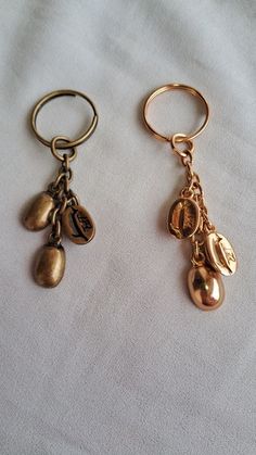 two gold key chains with charms attached to them on a white cloth covered tablecloth