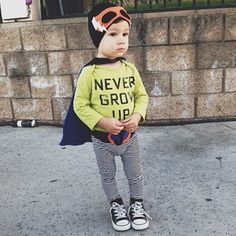 a young boy wearing a yellow shirt and striped pants standing in front of a brick wall